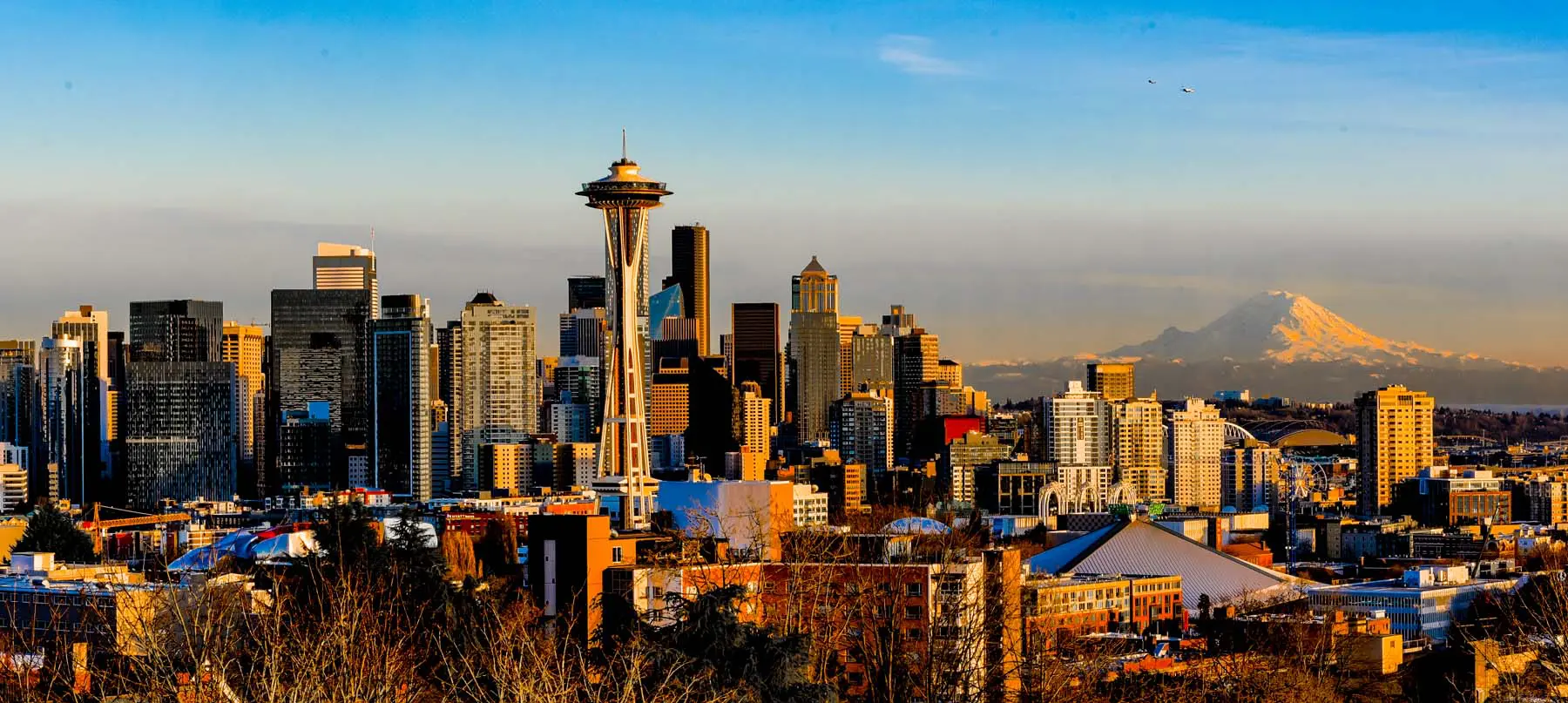 Golden hour view of Seattle skyline featuring the iconic Space Needle, downtown high-rises and distant Mount Rainier, conveying urban life, Pacific Northwest landscape and architectural contrast at sunset.