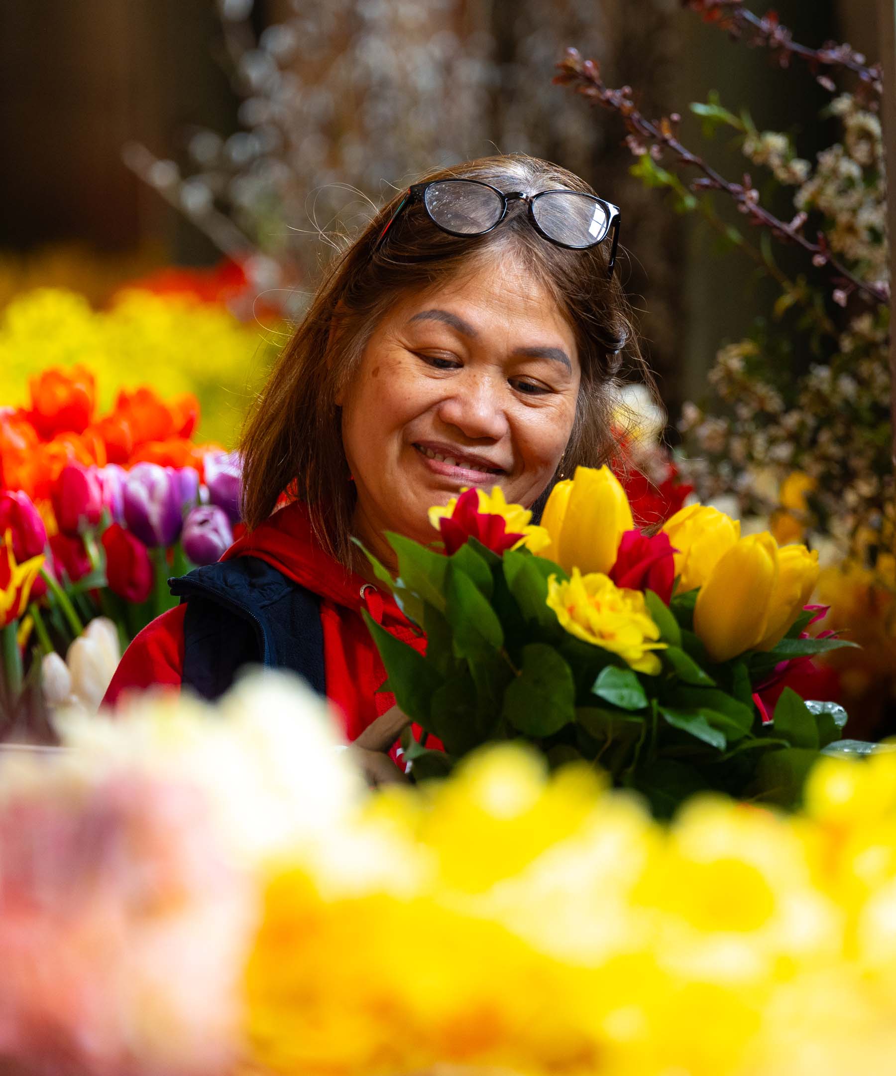 Beautiful Asian Flower Vendor Woman Choosing Colorful Tulip Bouquet At Busy Pike Place Market Flower Market in Seattle inspects a vibrant bouquet of yellow and red tulips at a bustling flower market, surrounded by colorful blooms and springtime atmosphere, conveying joy and simple everyday beauty.
